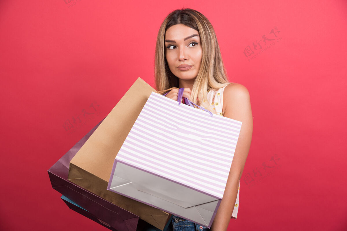 年轻红墙上一个拿着购物袋 表情中性的女人购物购买女孩