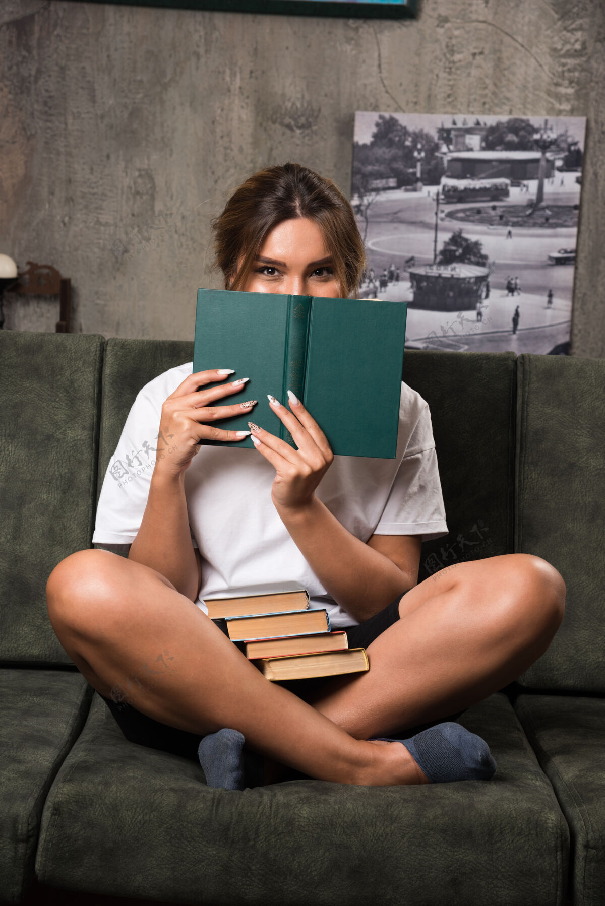 放松年轻女子躲在沙发上的书后面公寓女人积极