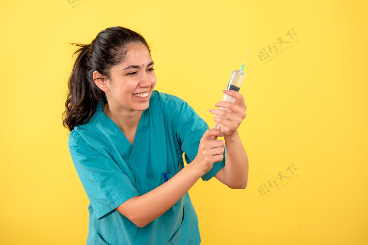成人正面图黄色背景上带注射器的快乐年轻女医生年轻女医生肖像微笑
