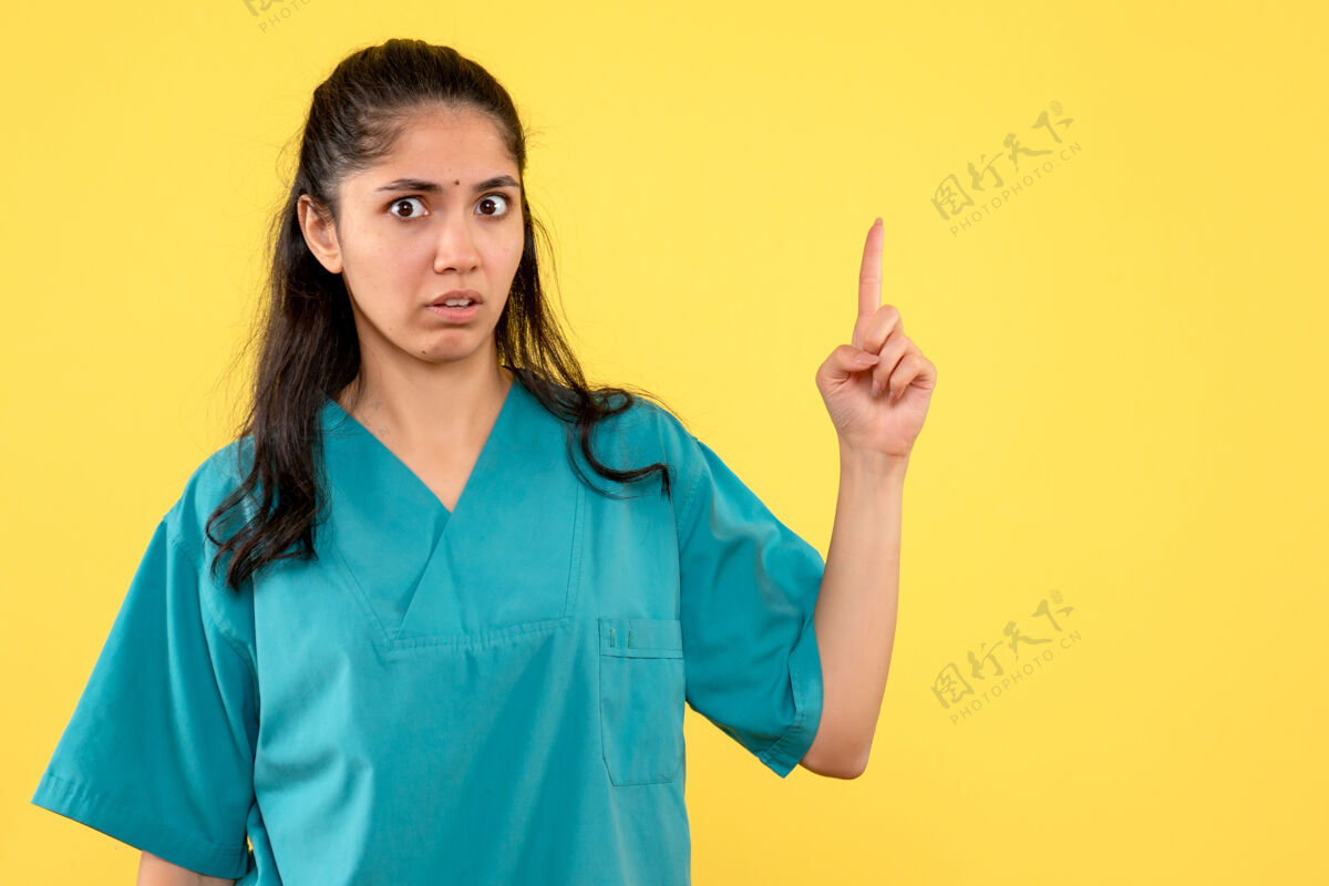 前面前视图困惑的女医生穿着制服 手指指向黄色背景护理微笑听诊器