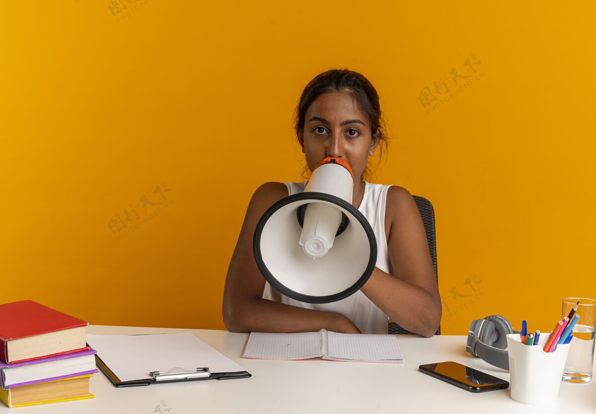 年轻人坐在书桌旁拿着学习用具的年轻女学生用扩音器讲话女人橙色工具
