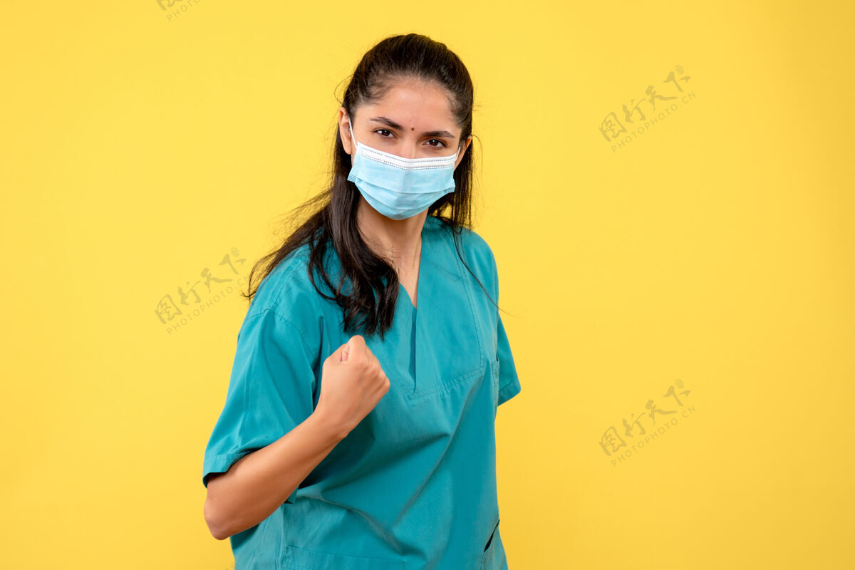女医生前视图确定女医生在黄色背景上展示她的拳头冲压漂亮面具