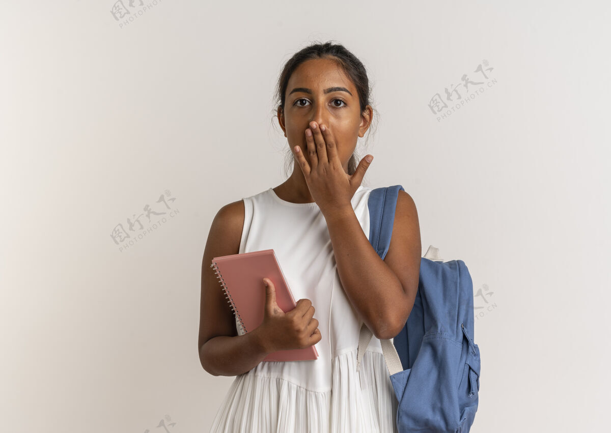 盖害怕的年轻女学生背着背包拿着笔记本 用手捂住嘴巴害怕穿背包