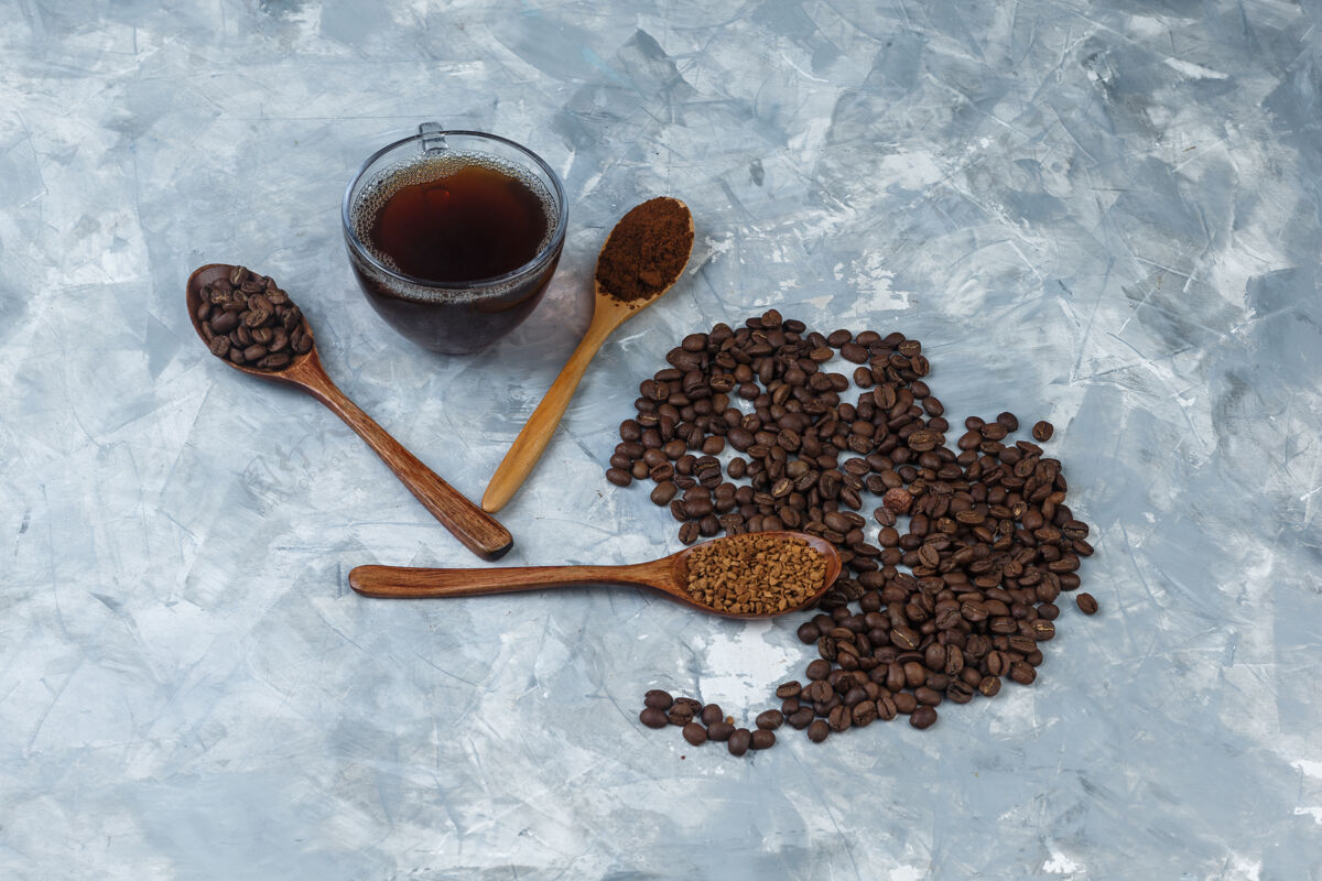 泡沫高角度观看咖啡豆 一杯咖啡加速溶咖啡 咖啡粉 咖啡豆放在浅蓝色大理石背景上的木勺里水平人水平热