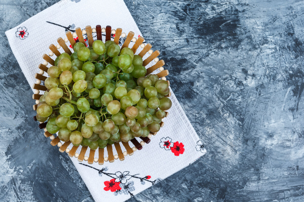 多汁绿色的葡萄在一个篮子里平放在肮脏的石膏和厨房毛巾的背景季节酒厂葡萄藤