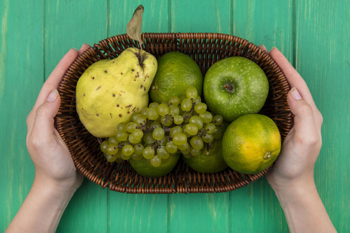 水果俯视图：一个女人拿着绿色的苹果 梨 橘子和葡萄 放在绿色的墙上的篮子里苹果梨景观