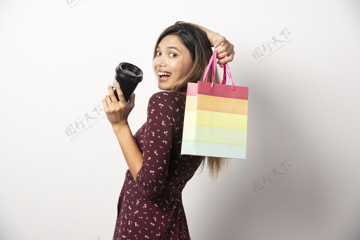 模型年轻女子拿着一个小购物袋和一杯饮料在白墙上女士购物人