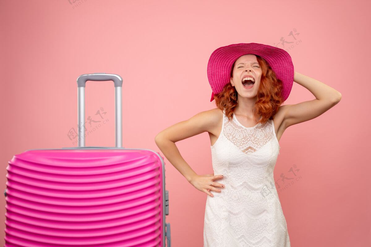 时尚年轻的女性游客与粉红色的帽子和粉红色的墙壁上的包的正面视图夏天包可爱