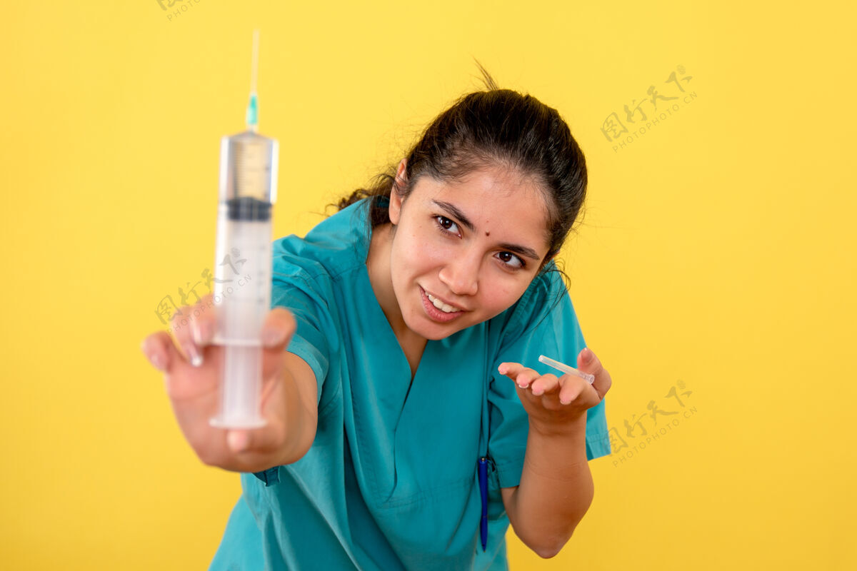 容器黄墙上拿着注射器的年轻女医生的正视图刷子仪器瓶盖