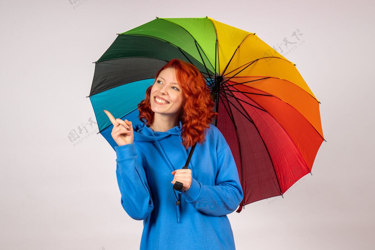 伞白色墙壁上带着彩色伞的年轻女性的正视图年轻女性掩护庇护所
