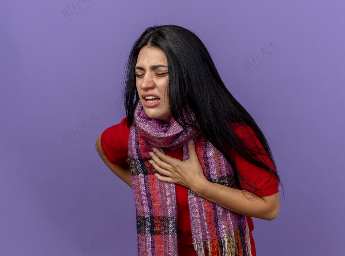 疼痛疼痛的年轻白种人生病的女孩戴着围巾把双手放在胸前和背上闭上眼睛隔离在紫色的墙壁与复制空间年轻紧闭磨损