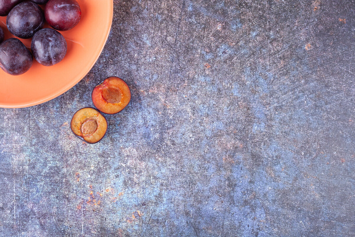 多汁一束新鲜的紫李子放在橙色的盘子里天然有机水果