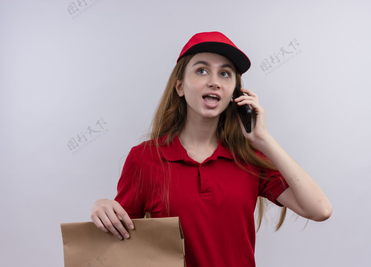 电话穿着红色制服的年轻送货女孩手拿纸袋 在与世隔绝的白墙上讲电话女孩制服年轻