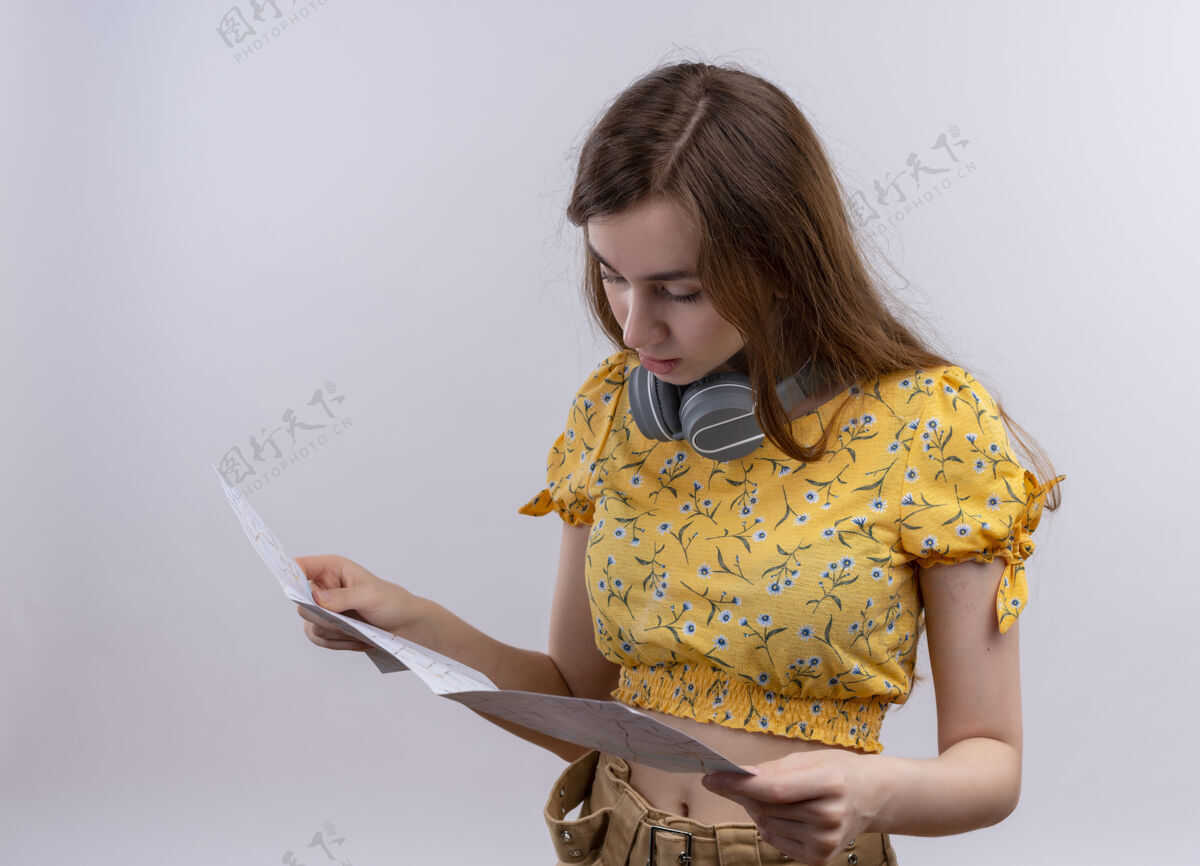 女人年轻的女孩戴着耳机在脖子上 拿着地图 看着孤零零的白墙上女孩年轻戴着