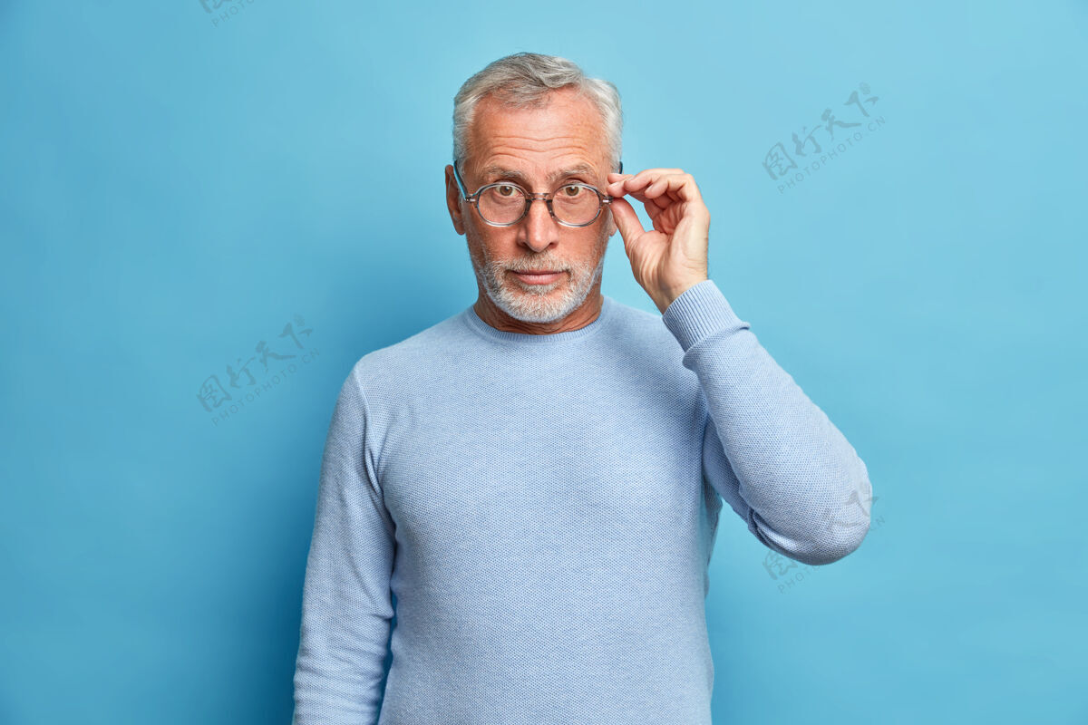 难以置信摄影棚拍摄的惊讶的成熟男子看与奇迹戴眼镜和休闲套头衫听到令人震惊的消息隔着蓝色墙壁印象深刻的奇妙事件手模特头