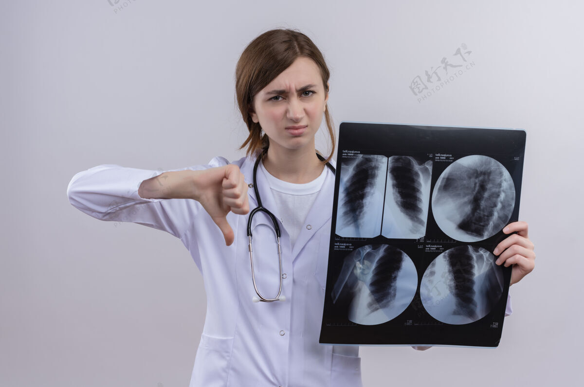 穿年轻的女医生穿着医用长袍 戴着听诊器 拿着一张x光片 大拇指朝下躺在隔离的白墙上女按住长袍