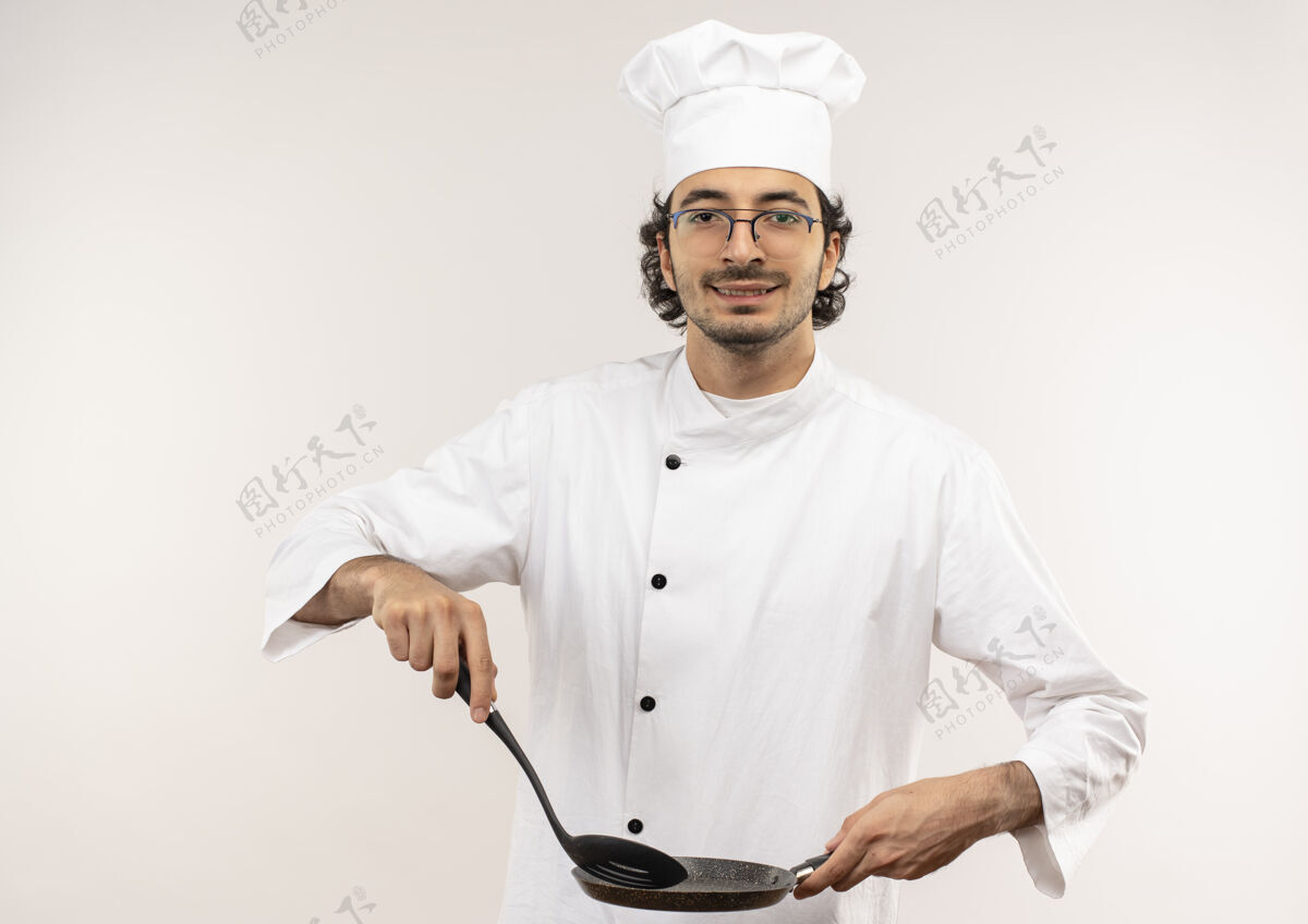 平底锅年轻的男厨师穿着厨师制服 戴着眼镜 手里拿着抹刀和煎锅 隔离在白色的墙上薯条抹刀请穿