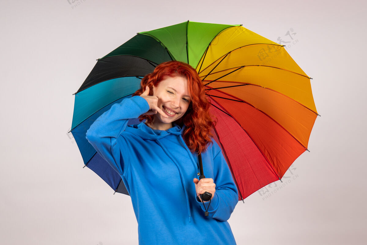 伞白色墙壁上带着彩色雨伞的年轻女性的正视图保护掩护雨天气