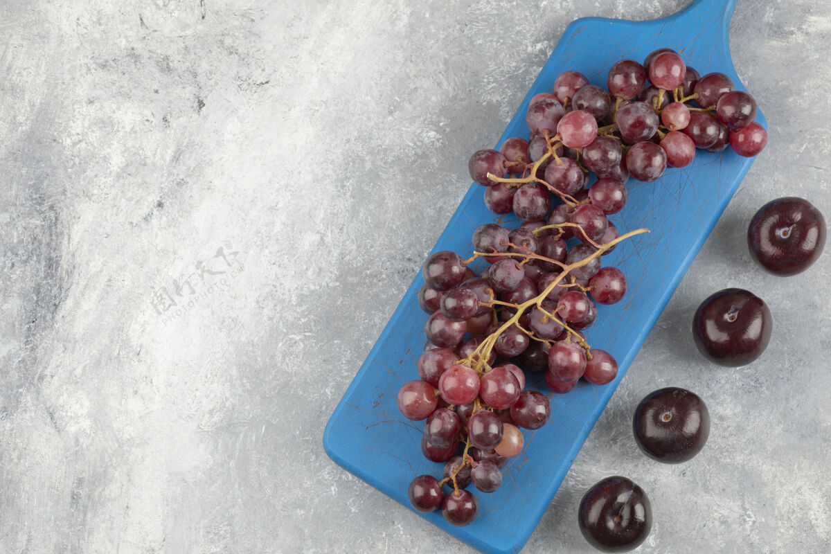 葡萄红葡萄放在蓝色的砧板上 新鲜的李子放在大理石表面一串水果多汁