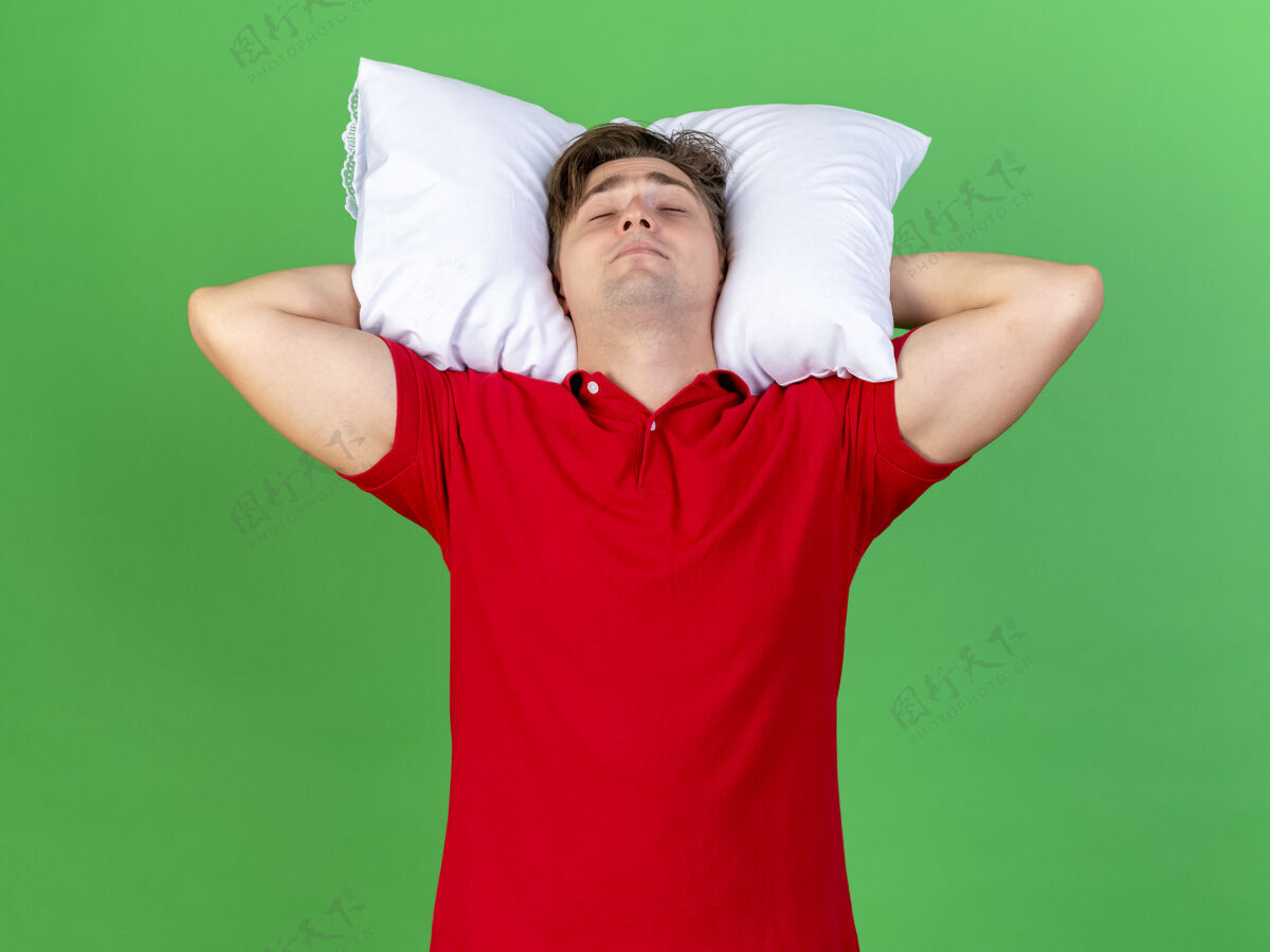 病年轻英俊的金发病男子抱着枕头在头下假装睡在绿色背景隔离年轻抱头