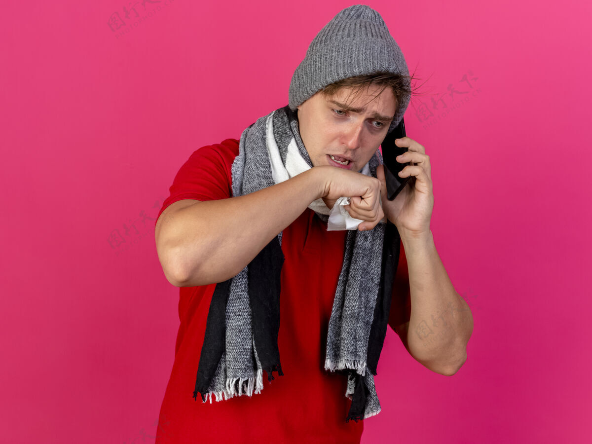 围巾弱小的年轻英俊的金发病患戴着冬天的帽子和围巾讲电话拿着餐巾把手放在嘴边看着被隔离的深红色背景和复印空间虚弱英俊餐巾
