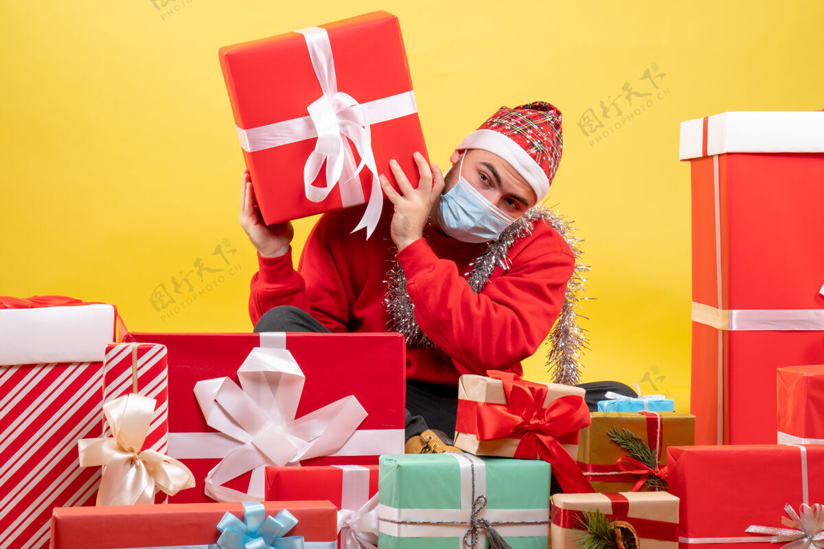 圣诞节正面图：坐在黄色背景上的年轻男性礼物坐着年轻的男性背景