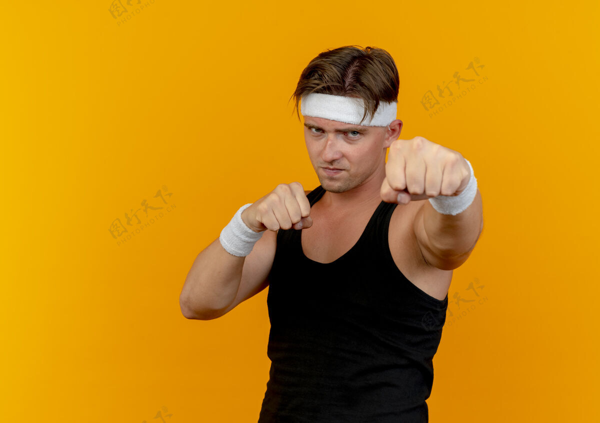 手势自信的年轻帅气的运动型男子戴着头带和腕带做拳击手势孤立的橙色与复制空间拳击帅气男人