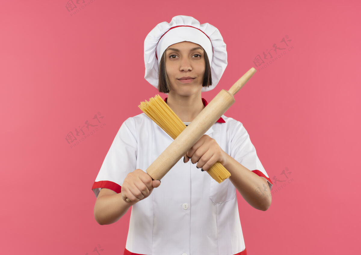 信心自信的年轻女厨师穿着厨师制服 用意大利面和擀面杖做手势 粉色上有复制空间意大利面空间粉红