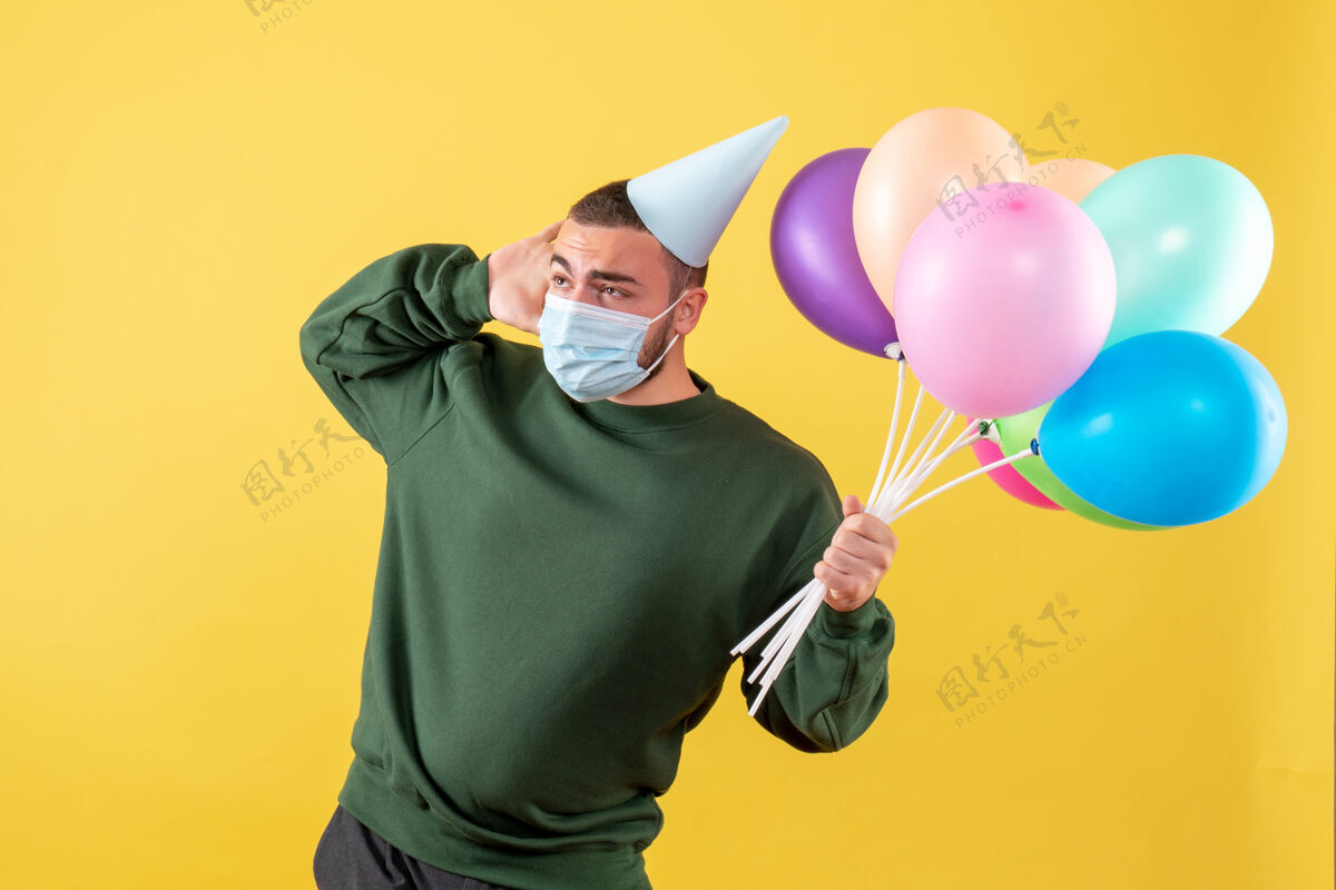 气球正面图黄色背景上手持彩色气球的年轻男性喜剧演员乐趣年