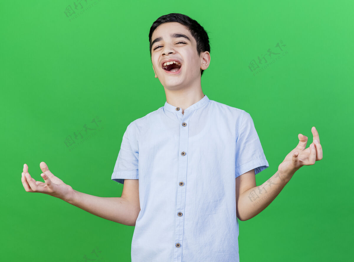 年轻快乐的年轻白人男孩看着相机 在绿色的背景下显示出孤立的空手快乐相机手
