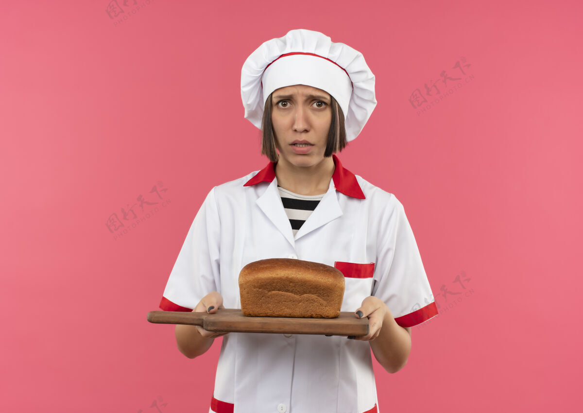 烹饪焦急的年轻女厨师穿着厨师制服 手里拿着砧板 上面有面包 粉红色上有单独的复印空间焦虑粉女