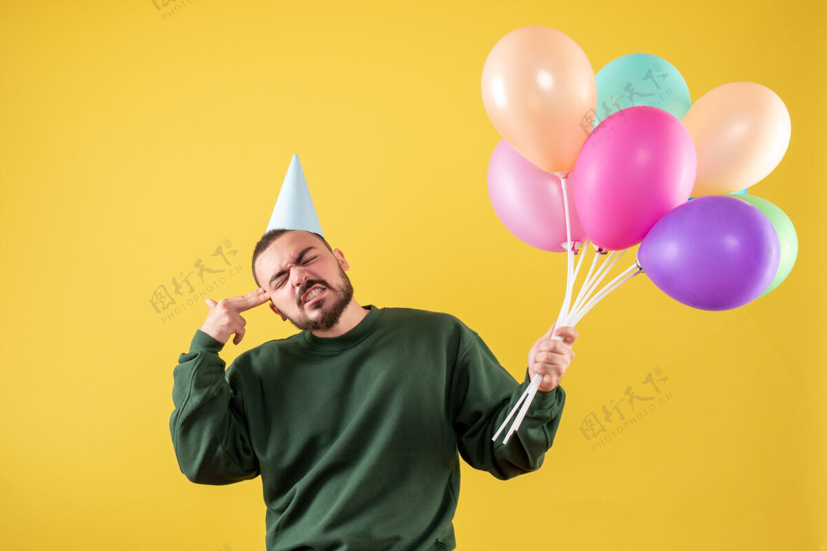 气球正面图黄色背景上手持彩色气球的年轻男性背景聚会年
