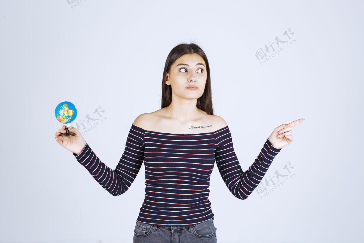 地图穿着条纹衬衫的年轻女子拿着一个迷你地球仪指着某处人成人地理
