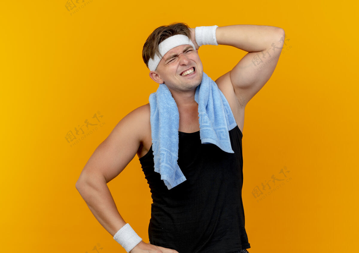 封闭疼痛的年轻英俊的运动型男子戴着头带和手镯 脖子上围着毛巾 手放在头上 闭着眼睛孤立在橙色上戴眼睛脖子