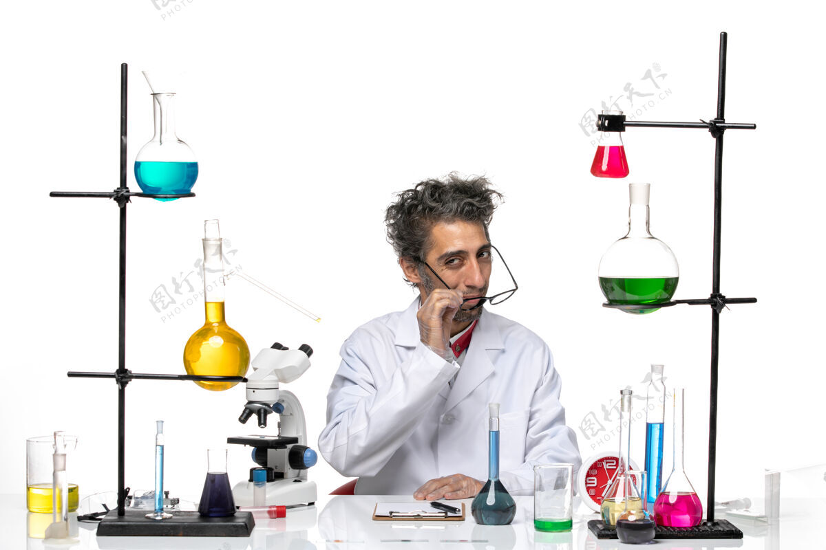 职业前视图穿着白色医疗服的男科学家坐在桌子前 带着解决方案实验室前台桌子