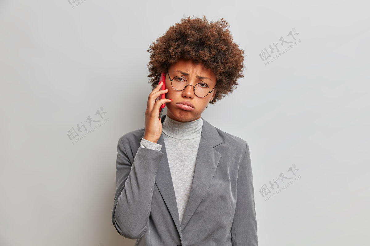 室内疲惫悲伤的卷发女商人 讲电话 穿着时髦的正装 谈吐枯燥 神情不愉快 疲倦叹息电话压力麻烦