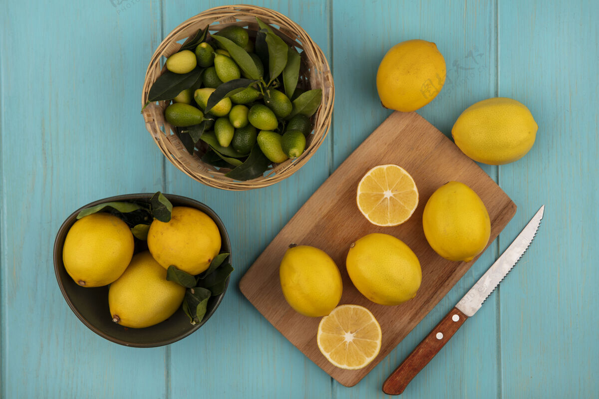 板碗上的圆形柠檬的俯视图 柠檬被隔离在木制厨房板上 蓝色木制墙上的桶上有一把带金盏花的刀切片厨房柠檬
