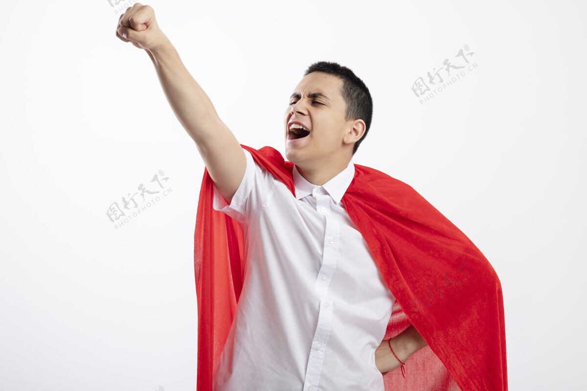 向上自信的年轻超级英雄男孩 穿着红色斗篷 手放在腰上 看起来笔直地举起拳头 孤立地站在白色背景上 留有复制空间提高信心拳头