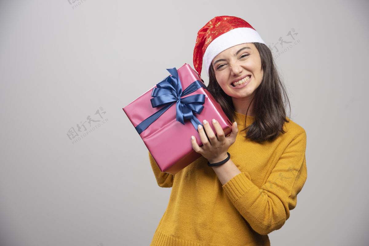 年轻戴着圣诞帽拿着礼品盒的快乐女人漂亮庆祝圣诞老人