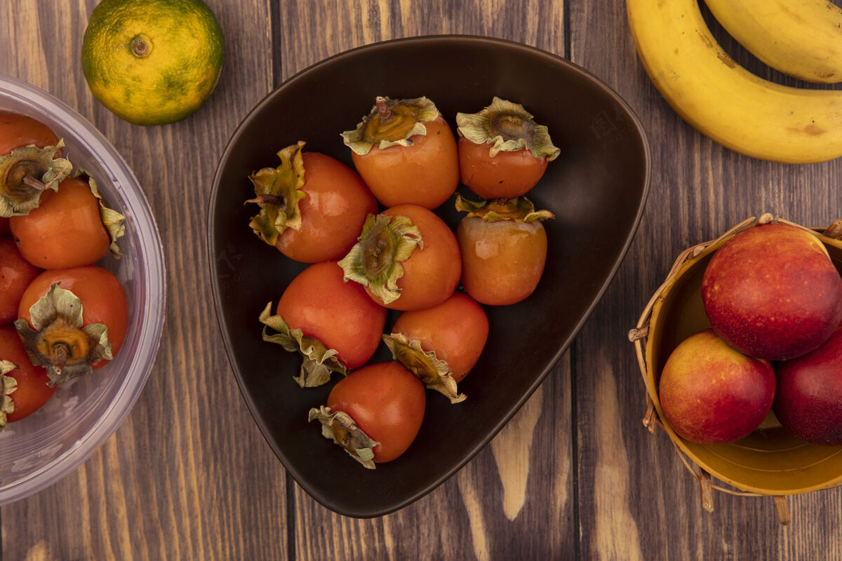桃子一个碗上的多汁柿子的俯视图 桶上放着桃子 木墙上隔离着香蕉观点多汁柿子
