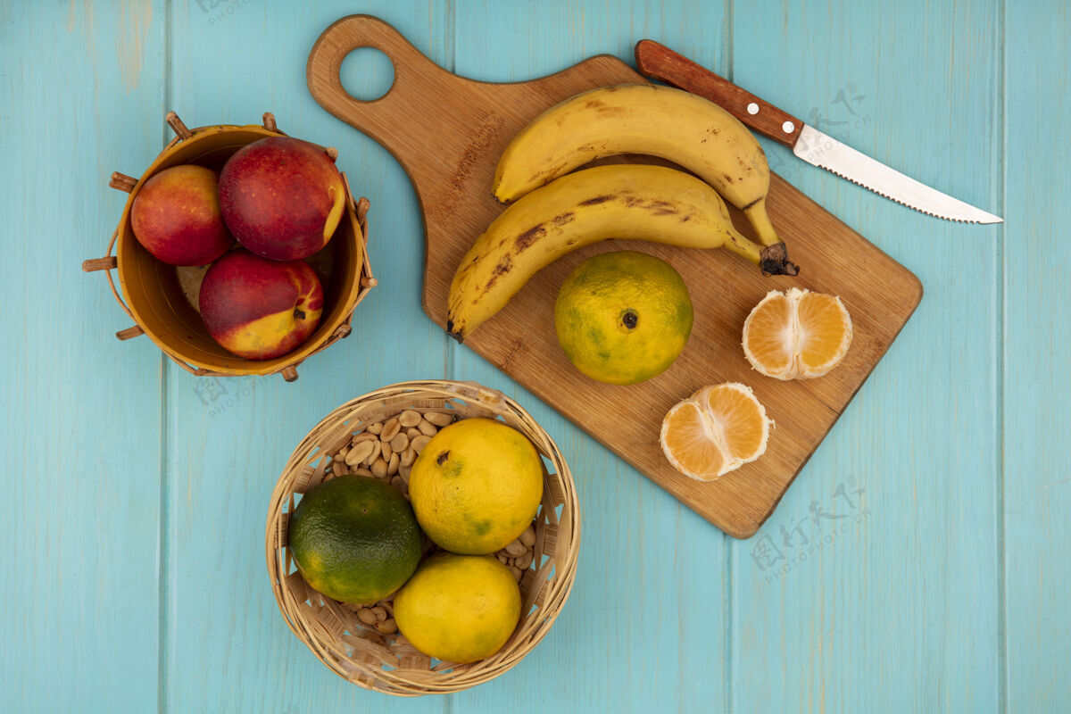 食物新鲜的整个和半个橘子在一个木制的厨房板上的俯视图 在蓝色的木墙上 香蕉和桃子放在桶上的刀橘子柑橘桃子