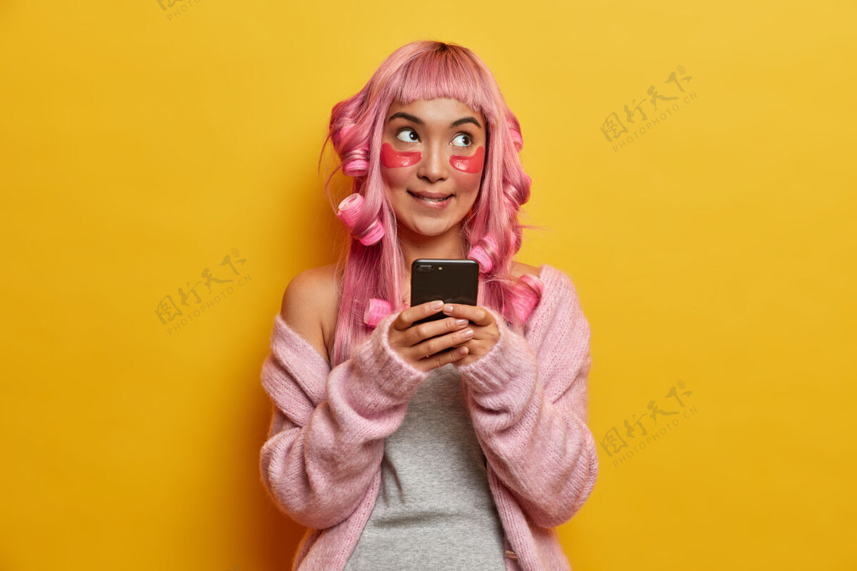 思想体贴的亚洲女人做发型 用卷发器 美容胶原蛋白贴片 手里拿着手机设备思考卷发器