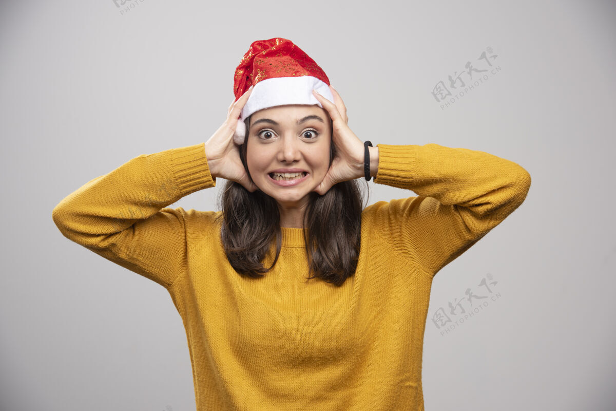 黑发戴圣诞帽的女人把脸贴在灰色的墙上人表情圣诞节