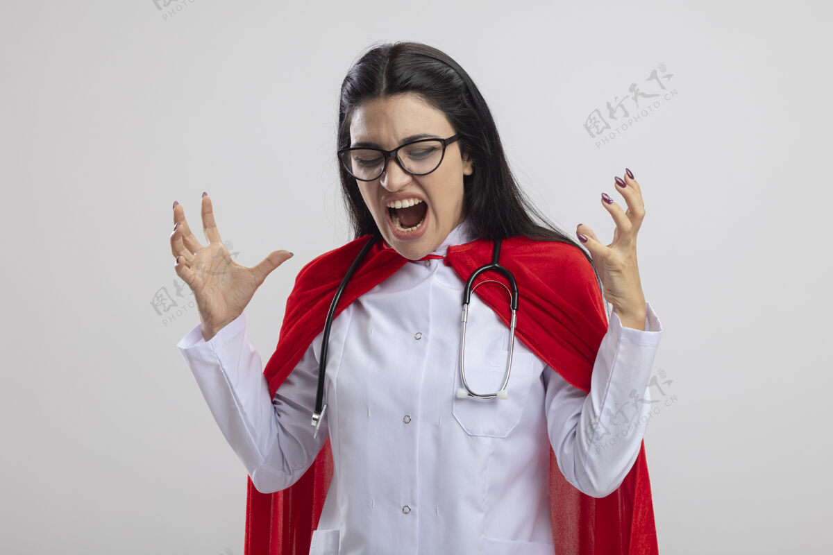 穿愤怒的年轻白种人超级英雄女孩戴着眼镜和听诊器双手举在空中尖叫着看着白色背景下的孤立尖叫女孩白色