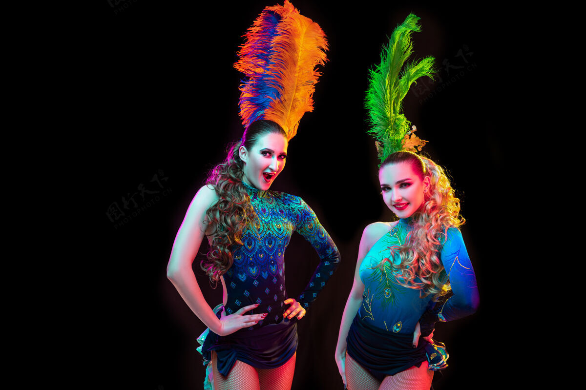人类美丽的年轻女子在狂欢节 时尚的化装服装与羽毛的黑色背景在霓虹灯下庆典神秘传统