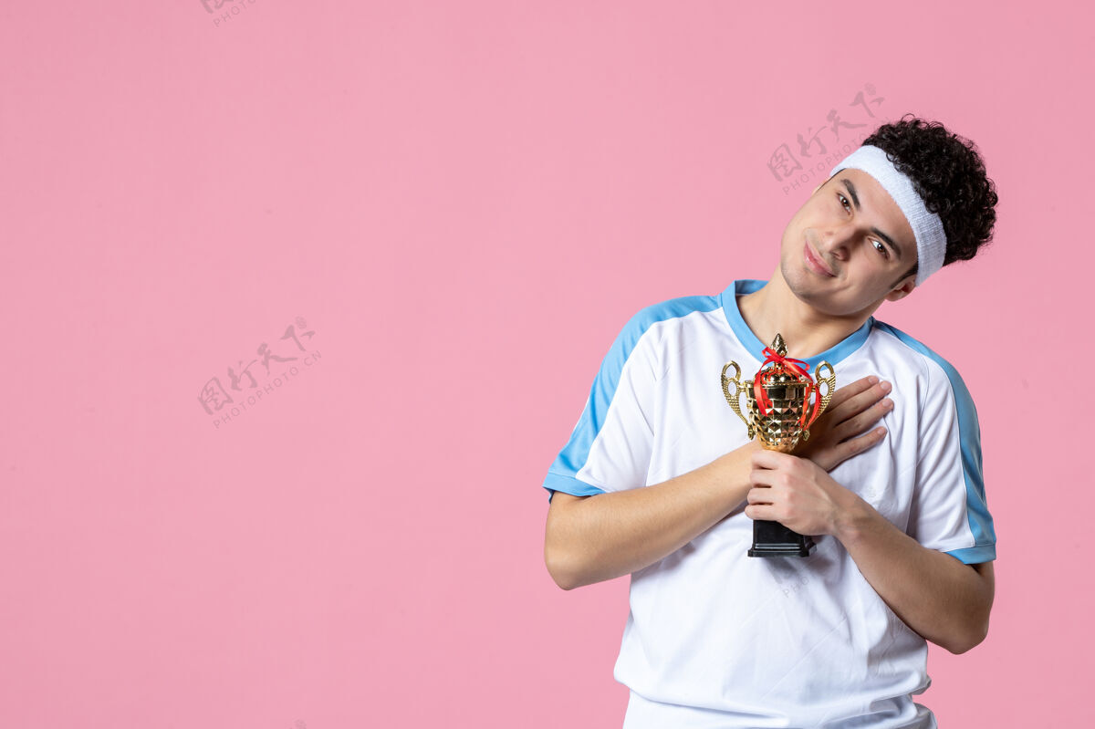 正面正面图：穿着运动服的快乐的年轻球员拿着金杯成功粉色胜利