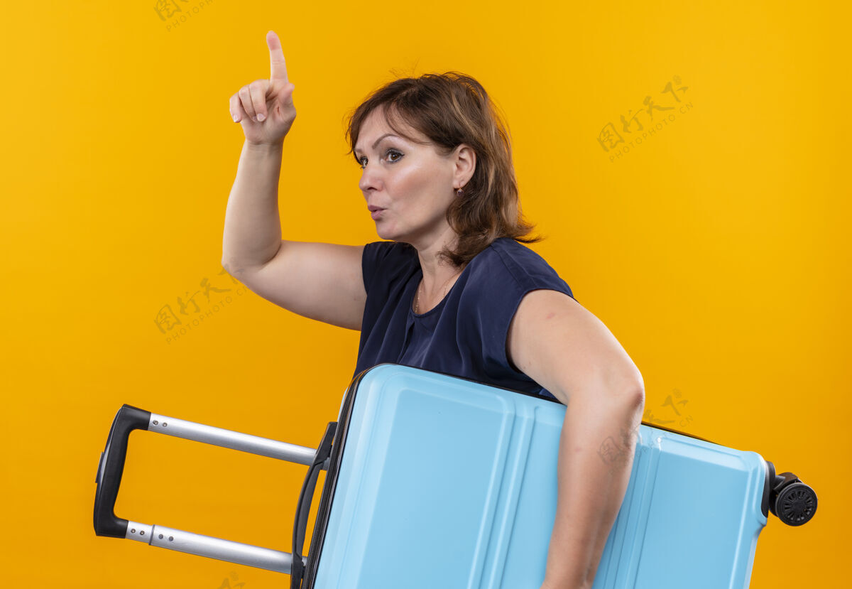 思考看着身边想着的中年旅行家女子拿着手提箱指着孤零零的黄墙上壁板女人手提箱