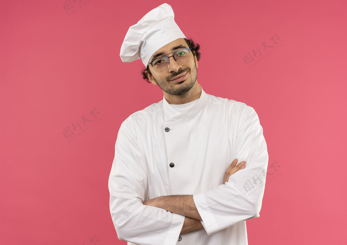 眼镜面带微笑的年轻男厨师身穿厨师制服 戴着粉红色交叉双手的眼镜粉色微笑背景