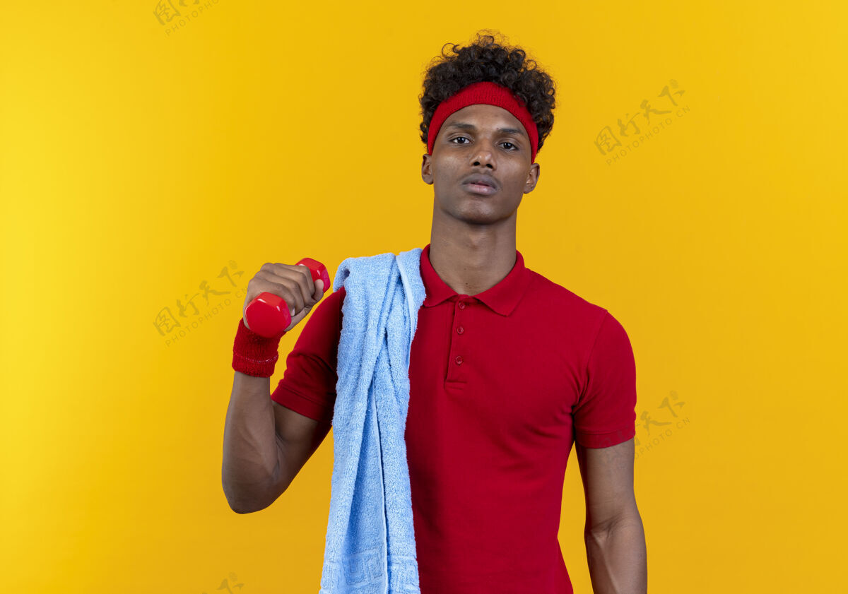 头带自信的年轻美国黑人运动男子戴着头带和手环举着哑铃 肩上拿着毛巾隔离在黄色的墙上腕带非裔美国人穿