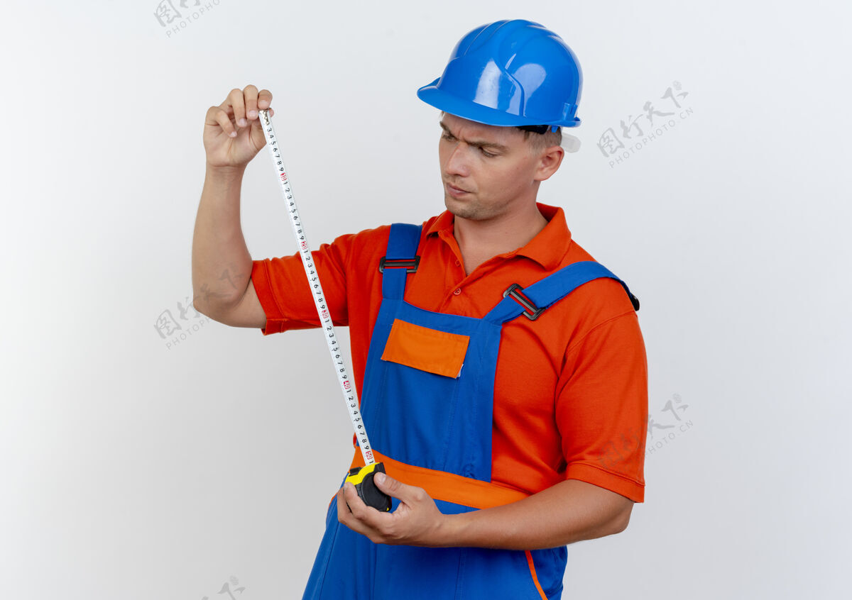 胶带想着年轻的男建筑工人穿着制服 戴着安全帽 手里拿着白色的仪表盘年轻头盔建设者